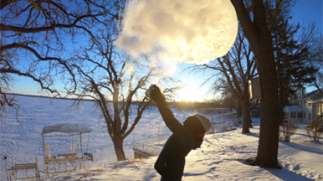 A person throwing boiling water into freezing air. The boiling water appears to have turned into a cloud.
