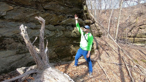 Image of man gesturing towards a rock face.