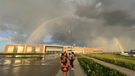 A rainbow in front of dark clouds over a school building.