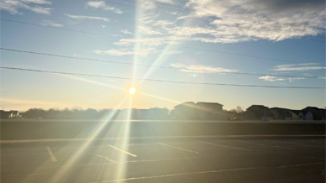 A sunrise over a line of trees and buildings.