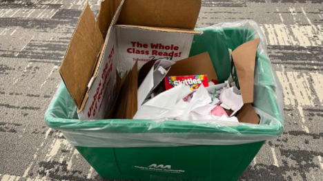 A recycling bin with paper, cardboard, wrappers, and other items in it.