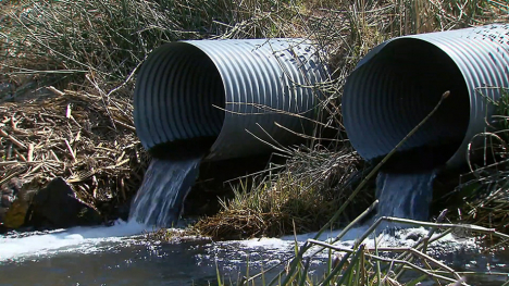 Image of water draining from pipes in a field.