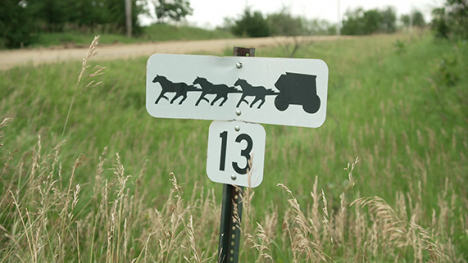 A horizontal white sign with a black drawing of a team of horses pulling a large coach above a square white sign with the number 13 in black.