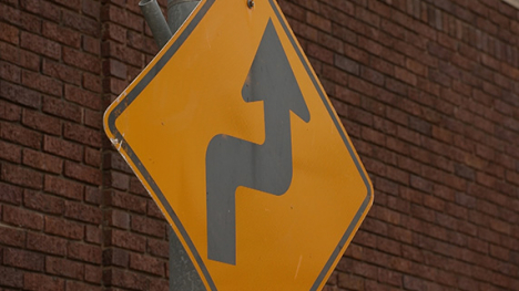 A yellow diamond-shaped road sign with an arrow that points up, to the right, then up again.