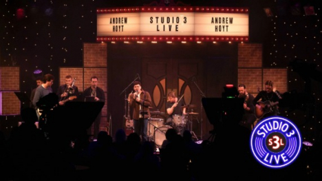 A dark stage with a band playing and a bright marquee above them.