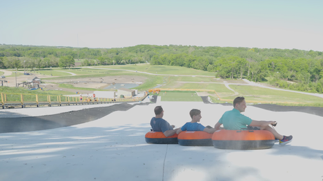 three people go down a snowless tube hill on orange intertubes