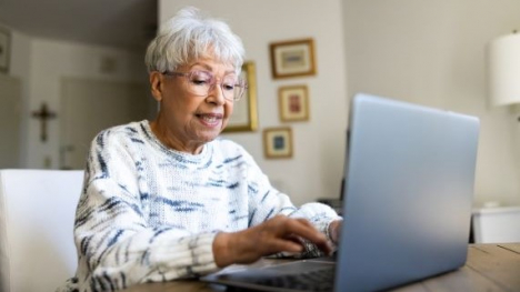 Woman with glasses typing on a laptop at a wooden table.