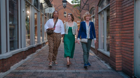 Three women, the main characters of the program, walking down an alleyway. 