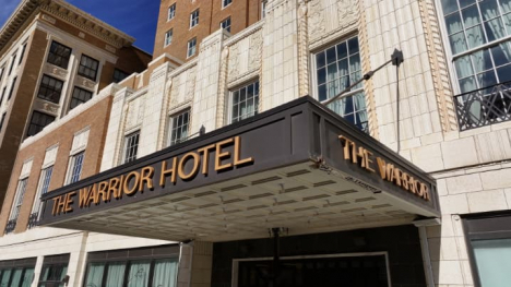 Historic hotel entrance with a black marquee reading “THE WARRIOR HOTEL” on a cream stone and brick building.