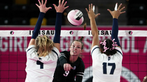 Two teenage girls attempt to block a volleyball from coming over the net.