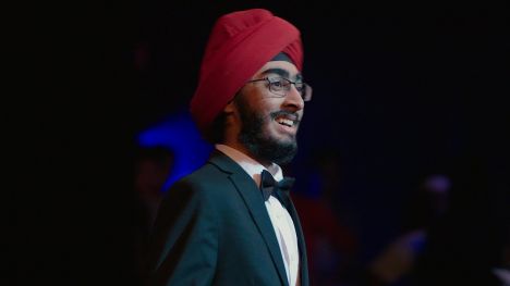 JJ Singh Kapur wearing a red turban and speaking in an auditorium.