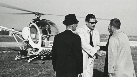 Iowa Governor Harold Hughes shakes hands with another man while standing in front of a helicopter. Two other men stand at their sides.