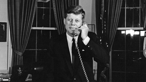 President John F. Kennedy standing while on the telephone.