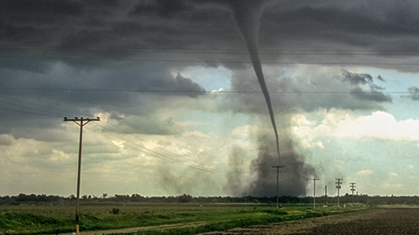 A tornado tears across a rural field near a row of powerline poles.