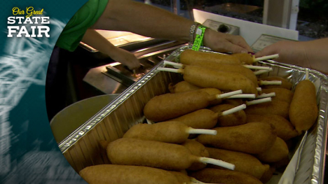 Two women lift a large tray of corn dogs