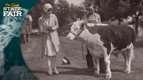 A man stands next to a cow while a woman writes on a clipboard