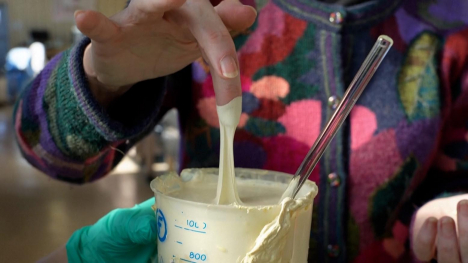 A person pulls their finger out of a container with an alternative rubber substance dripping from their finger.