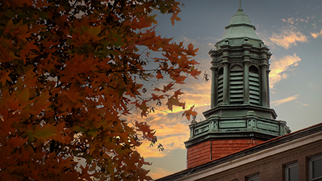 A building at the Iowa School for the Deaf behind a tree in fall color.