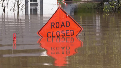 Road Closed sign partially submerged underwater.