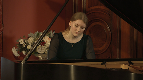 A young woman in a green dress plays music on a grand piano.
