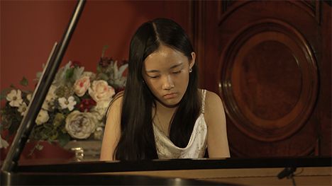 A young woman in a white dress plays music on a grand piano.