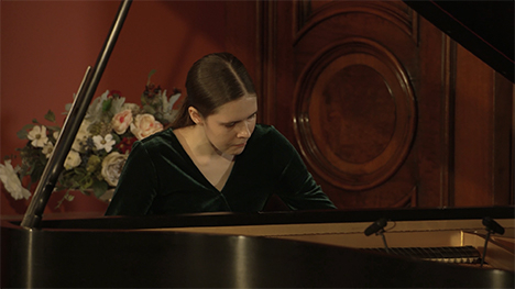 A young woman in a green dress plays music on a grand piano.