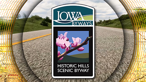 Iowa Byways: Historic Hills Scenic Byway sign overlayed on a road background.