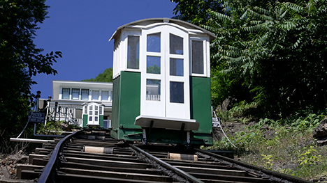 A small green and white outdoor elevator moves a steep hill on railroad type tracks