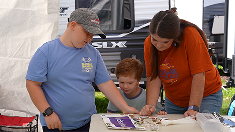Two boys and their mom look at Iowa State Fair items on a table at their campsite.