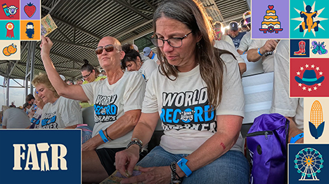 A man lifts his winning lottery scratch ticket while a woman next to him scratches off her lottery ticket. They sit in the bleachers with other lottery scratch ticket event participants.