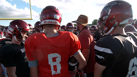 High school football coach surrounded by his team 