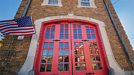 Hose Company No. 4 red firehouse doors. An American flag, attached to the brick building, blows in the wind.