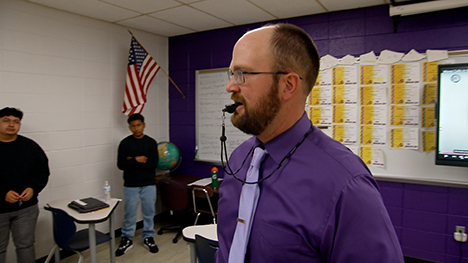 A classroom teacher has a whistle in his mouth as he instructs high school students how to officiate sporting events.