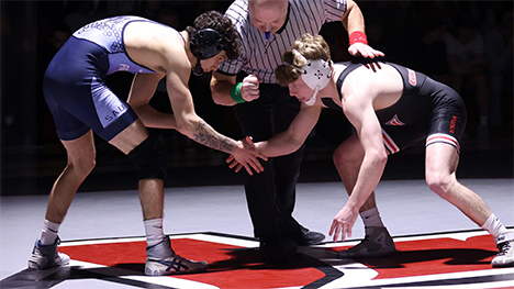 Two wrestlers shake hands just before the referee signals them to wrestle.