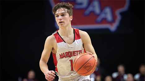 A high school boy basketball player running up the court dribbling a basketball in hand.