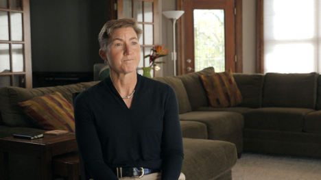 A person sits in a cozy living room with a sectional sofa and floor lamp.