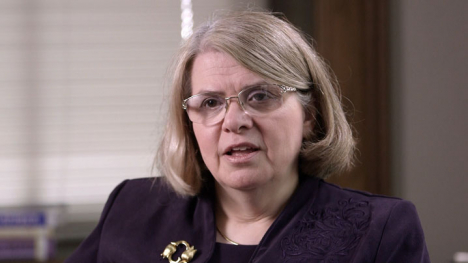 A woman in a purple blazer sits before the camera.