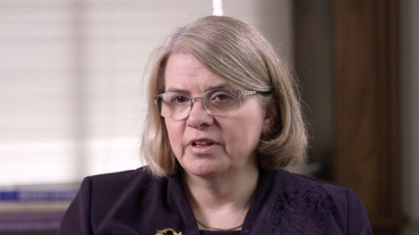 A woman in a purple blazer sits before the camera.