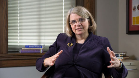 A woman in a purple blazer sits before the camera.