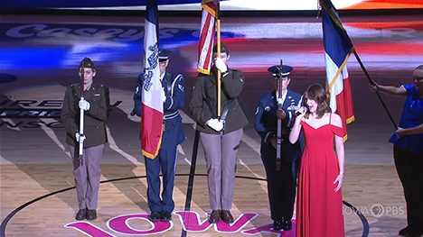 The national anthem is sung on the basketball court next to military personnel.