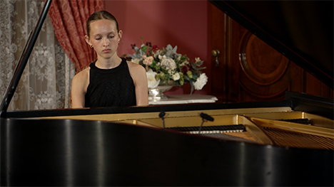 A young woman in a black dress playing at a grand piano.