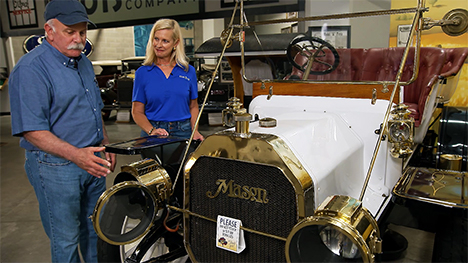 A car museum guide points out features of a white antique car to Road Trip Iowa host, Brooke Kohlsdorf.