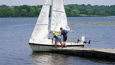 Two men board a small docked sailboat on Lake MacBride.