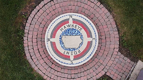 A top down view of a circular mosaic and brick platform. The mosaic has a compass rose on it, and the words, "Hawkeye Point" with an Iowa-like shape in the middle.