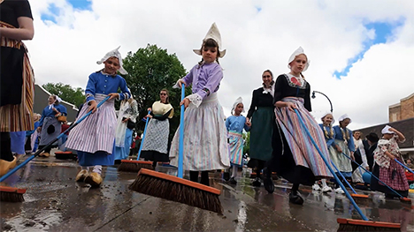 Dutch girls in wooden shoes push brooms through the streets.