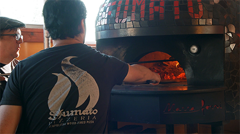 Two cooks tend to the pizzas baking in the oven.