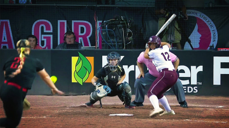 A girls softball game — a pitcher throws a softball towards a batter (over home plate). A catcher and umpire also await the ball. 