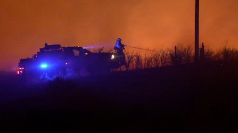 A firefighter stands beside an emergency vehicle as the Morrill Fire glows orange across the horizon.