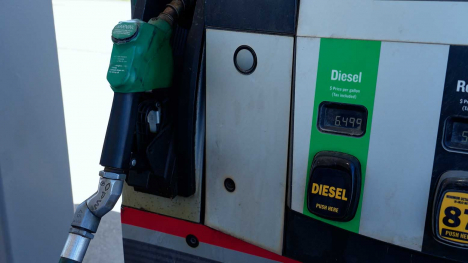 Green diesel nozzle hanging on a fuel pump beside a digital price display.