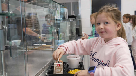 Student carries a lunch tray with milk and food through a school cafeteria line.
